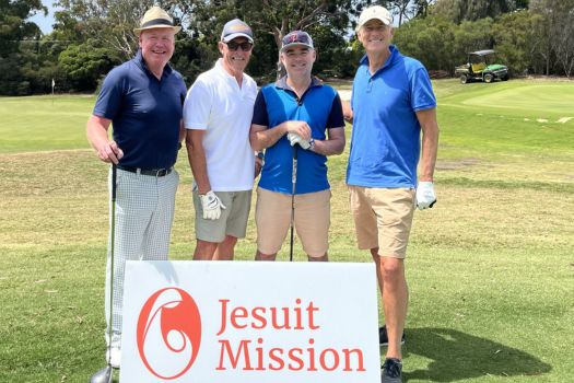 Four fundraising golfers standing behind a Jesuit Mission sign on the golf course