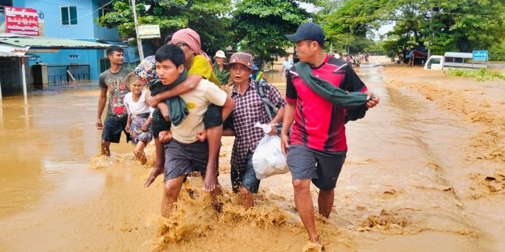 A family fleeing from flooding. One son carries his grandmother on his back.